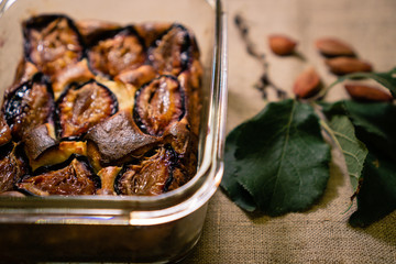 Cheesecake with plums baked in a transparent pan. Near the plum branch with leaves and plum bones