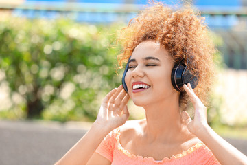 Beautiful African-American woman listening to music outdoors