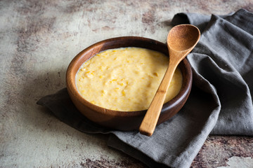 Corn porridge in wooden bowl with wooden spoon in vintage style on grey background