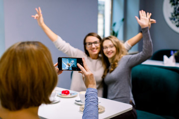 Women friends in cafe indoors. Two pretty women friends hugging, with hands up and posing for the...