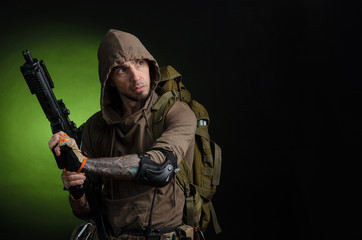 man Stalker with a gun with an optical sight and a backpack on a dark background with emotions looking, aiming, watching, sneaking