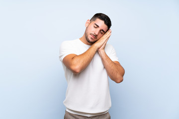 Caucasian handsome man over isolated blue background making sleep gesture in dorable expression