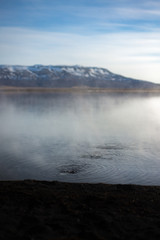 Steam Rises off of Hot Springs in a Lake in Iceland with Snowy Mountains in the Background