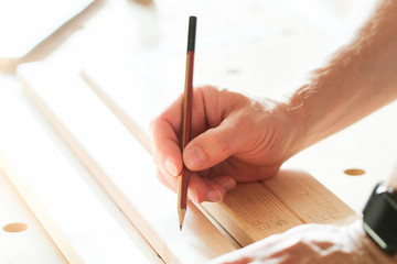 A carpenter applies marking with a pencil on a wooden block.