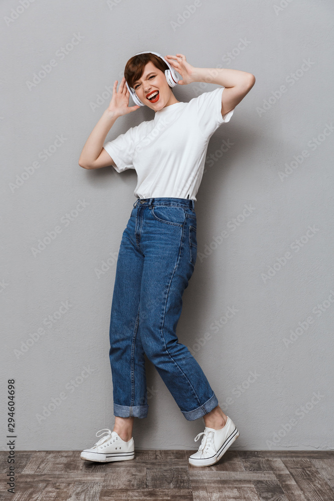 Wall mural Full length image of cheerful woman listening to music with headphones