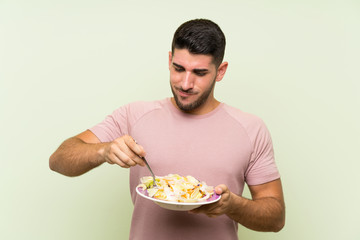Young handsome man with salad over isolated green wall
