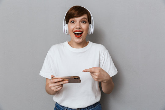Image of young woman wearing headphones playing games on cellphone