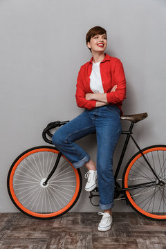 Full length image of pleased woman smiling and standing by bicycle