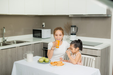 Asian children and her mom drink orange juice in the morning