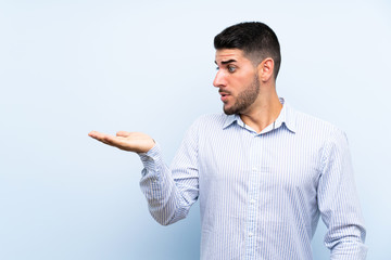 Fototapeta premium Caucasian handsome man over isolated blue background holding copyspace imaginary on the palm