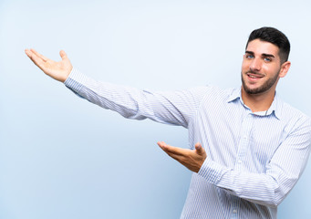 Caucasian handsome man over isolated blue background extending hands to the side for inviting to come