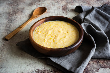 Sweet corn porridge in beautiful wooden bowl with wooden spoon in vintage style on grey background