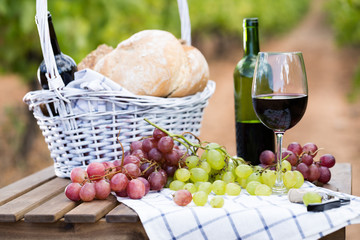 red wine ripe grapes and picnic basket on table in vineyard
