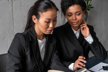 Two smart and beautiful business partners in dark suits discussing work at office table. Concept of international company and teamwork