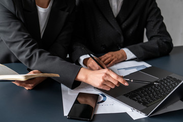 Hands of two businesswomen working together at office table and pointing at laptop screen. Concept of business partnership