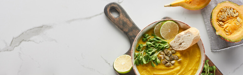 panoramic shot of autumnal mashed pumpkin soup on wooden cutting board on marble surface