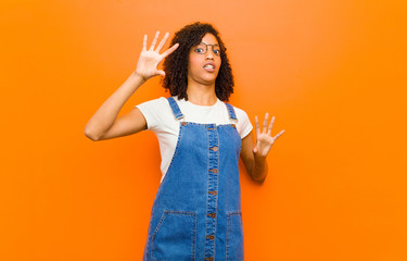 young pretty black woman feeling stupefied and scared, fearing something frightening, with hands...