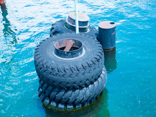 Large old black tires being used as bumpers at concrete dock, partially submerged in blue water