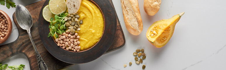 top view of autumnal mashed pumpkin soup in bowl on wooden cutting board on marble surface, panoramic shot
