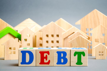 Wooden blocks with the word Debts and miniature houses. Debt concept for housing or mortgage. Real...