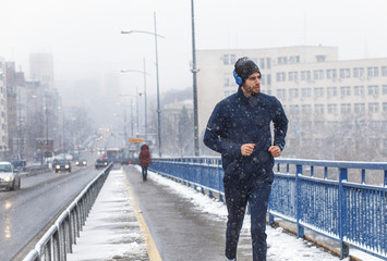 Young man running in city street at cold winter day.