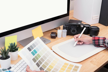 Graphic designer artist using graphics tablet drawing and looking at colour chart his work at desk in office.