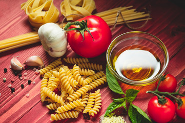 Tasty appetizing italian spaghetti pasta ingredients for kitchen cuisine with tomato, cheese parmesan, olive oil, fettuccine and basil on wooden brown table. Food Italian recipe homemade. Top view