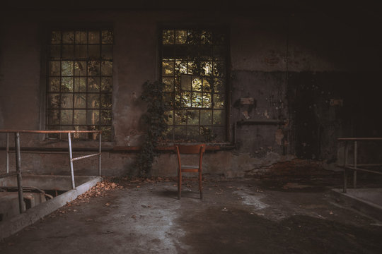 Wooden chair in front of an old and broken window within an abandoned building