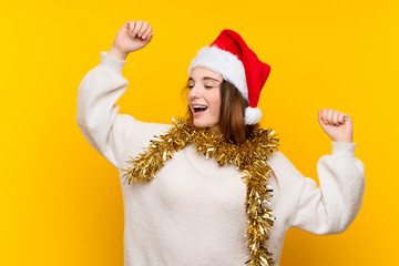 Girl with christmas hat over isolated yellow background celebrating a victory