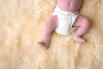 Newborn baby legs with white nappy, diaper on a fur background.