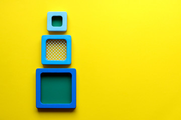 Geometry. Three blue squares on bright yellow background. Minimalism. Creative abstract concept. Educational wooden toys for children, learning shapes and colours shades