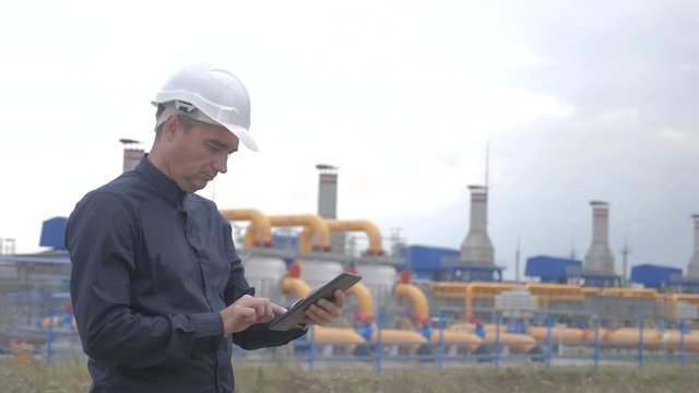 teamwork gas production station concept. lifestyle Engineering man standing writes documents on digital tablet white safety helmet. man engineer in helmet work at the station are studying on gas
