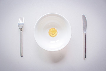 Concept image of Bitcoin Hard Fork (Block Chain). Golden Bitcoin on the plate with fork and knife. Cryptocurrency coin served on white table.