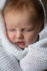 A one month old baby asleep wrapped in a white blanket