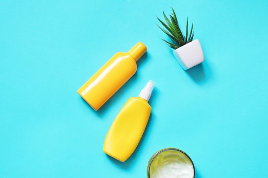 Flat lay photo beach essentials, skin care cosmetics with spf. Two yellow sunscreen bottles, moisturizing body cream and aloe on a blue background