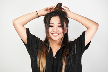 Fototapeta premium Pretty Kazakh Asian young woman in black with trendy bun of hair on head smiles and poses with stylish hairstyle isolated in white studio