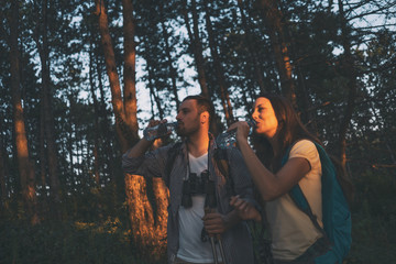 Young couple is hiking in forest. They are drinking water.