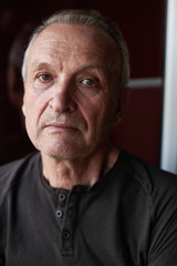 Portrait of serious handsome elderly man with gray hair, stylishly dressed , looking at camera against the background of window