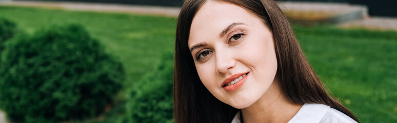 panoramic shot of attractive smiling young woman on street