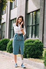 full length view of disabled woman holding smartphone with earphones on street