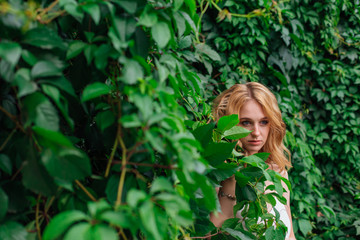 Fototapeta premium Portrait of a young beautiful woman, standing next to the wall of wild grape leaves.