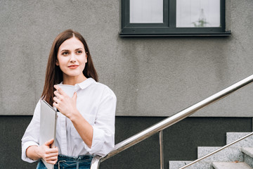 attractive young woman in white shirt holding laptop on street