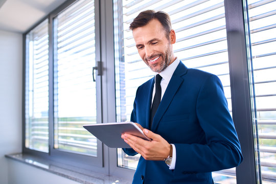 Happy businessman standing with tablet in office