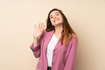 Young brunette girl with blazer over isolated background saluting with hand with happy expression