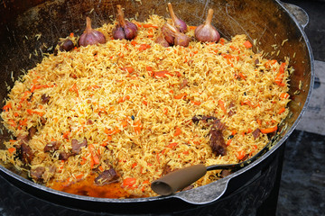 Big cauldron of asian traditional pilaf. Pilaf is cooking from rice with beef or lamb, carrot and spice. Plov close up. National food of Central Asia.