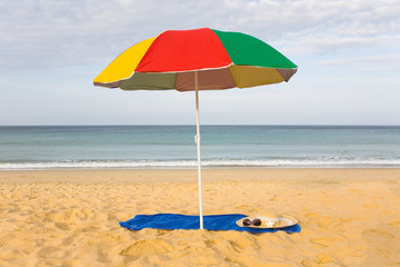 A beach umbrella over the bedspread on which glasses and a women's hat lie.
