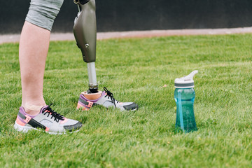 partial view of disabled sportswoman standing near sport bottle on grass