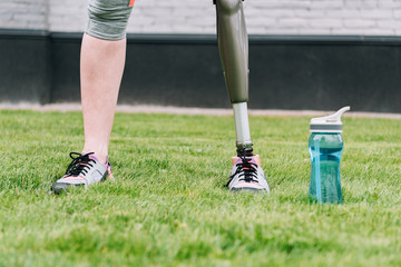 partial view of disabled sportswoman standing near sport bottle on grass on street