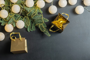 Christmas decorations with fir tree branches, shining garland, snowflakes and golden paper bags on black background with copy space for your text. Overhead flat lay