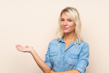 Young blonde woman over isolated background holding copyspace imaginary on the palm